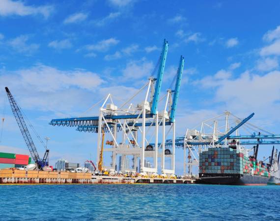 Cargo ship at Miami harbor with crane and blue sky over sea.